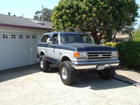 1989 Ford Bronco - Lifted 1989 Ford Bronco with two-tone paint parked in front of a garage.