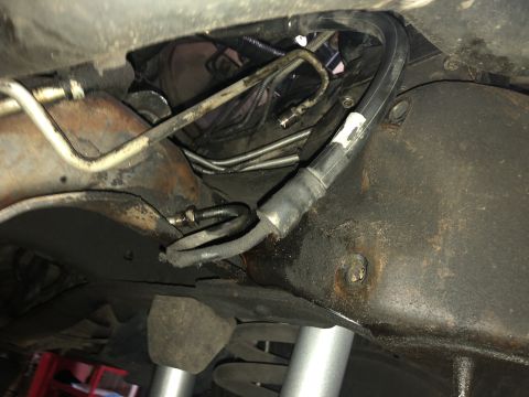 1995 Ford Bronco - Close-up of vehicle's underside, focusing on steering system hoses and metal tubing.