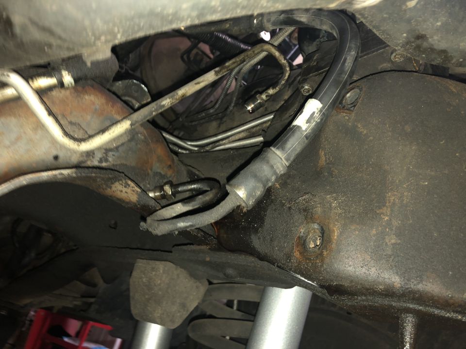 Underside view of vehicle's steering system components, showing hoses and metal lines