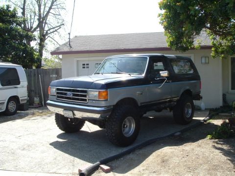 1989 Ford Bronco - This two-tone Ford Bronco is parked in front of a garage with a white van to its left.
