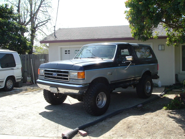Lifted black and silver Ford Bronco SUV on big tires parked in a driveway.