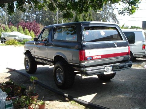 1989 Ford Bronco - A lifted, two-tone Ford Bronco is parked next to a white van in a driveway.
