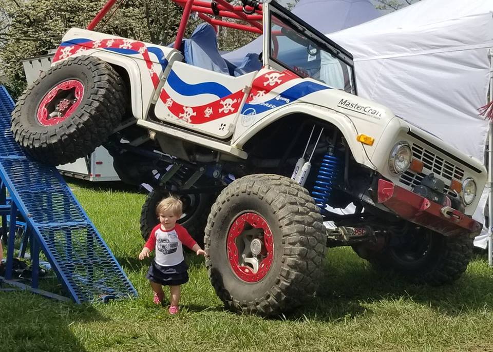 Kid next to a lifted white SUV with red and blue skull graphics and large off-road tires