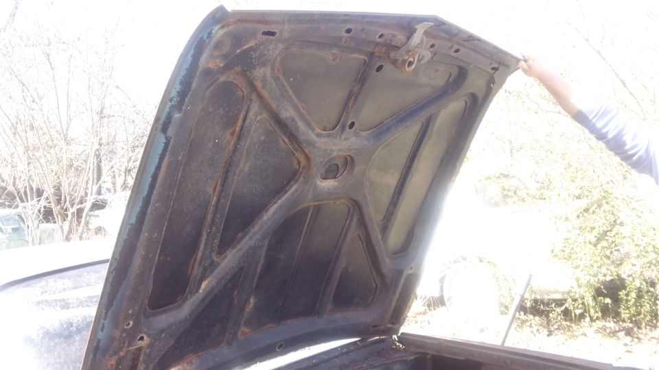 Underside of a dark-colored car hood, showing structural bracing and rust