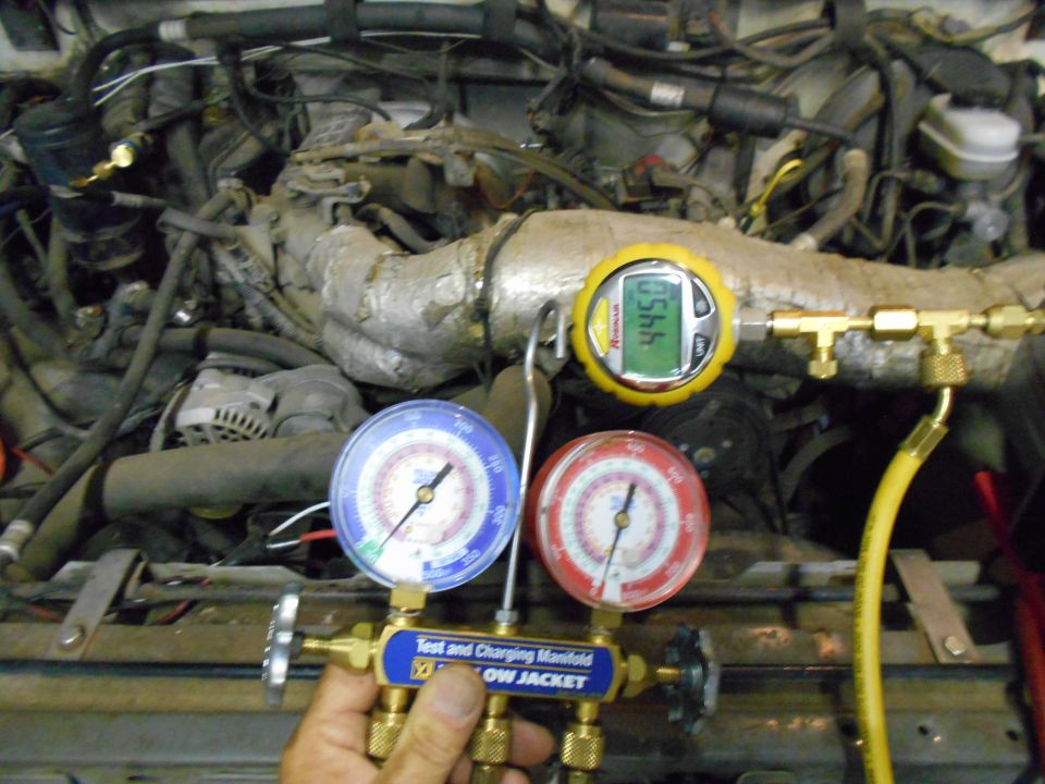 Engine bay with AC manifold gauges attached to hoses. Digital gauge reads 445.0