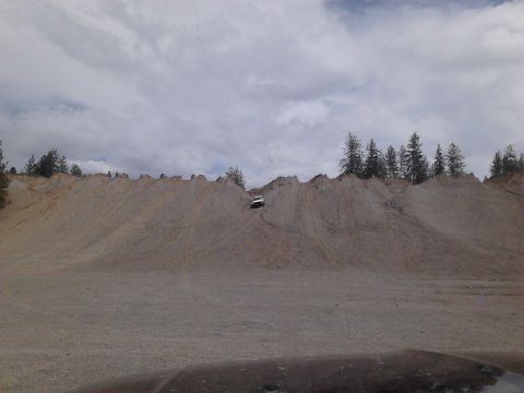 1995 Ford Bronco - A white SUV navigates a challenging ascent on a sandy embankment, with trees visible on the ridge above.