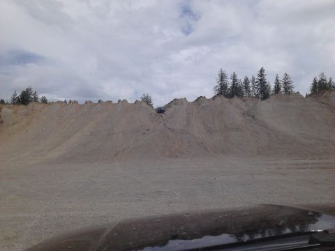 1995 Ford Bronco - A dark off-road vehicle navigates a challenging sandy incline, with trees visible on the ridge above.