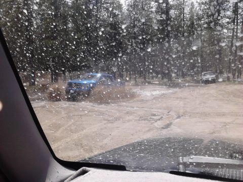 1995 Ford Bronco - Two vehicles navigate a wet, muddy path through a wooded area, with water droplets obscuring the view.