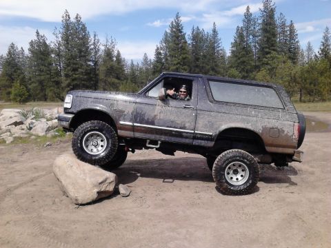 1995 Ford Bronco - A driver gives a thumbs up from inside a dirty Ford Bronco as it navigates an off-road obstacle.