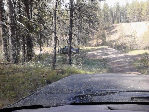 1995 Ford Bronco - A vehicle is parked off a dirt road in a wooded area, seen from the perspective of another vehicle.