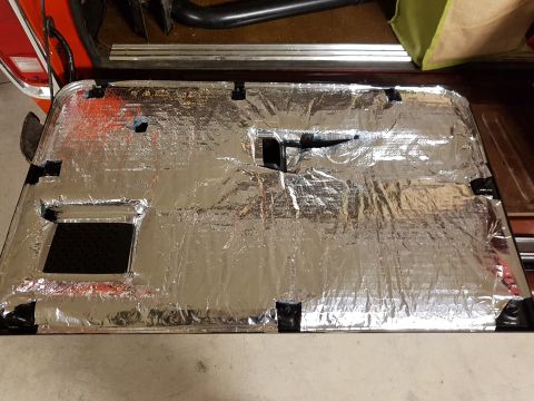 1978 Ford Bronco - A red vehicle's interior door panel is covered with silver insulation material and secured with black tape.