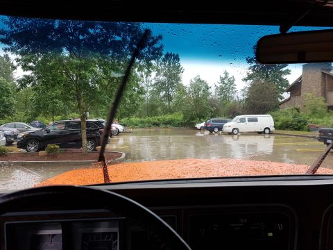 1978 Ford Bronco - Rainy day scene shows multiple vehicles parked in a flooded lot, viewed from inside another vehicle.