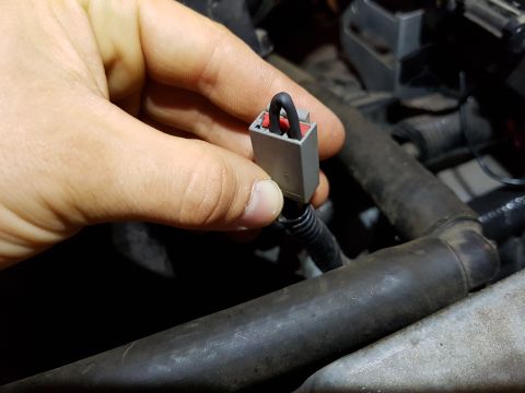 1978 Ford Bronco - A hand holds a gray electrical connector with red and black wires, likely part of an automotive repair or modification.