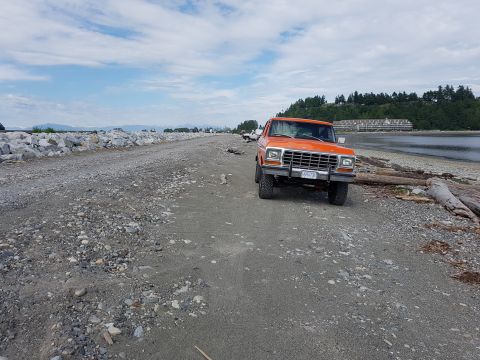 1978 Ford Bronco - A 1978 Ford Bronco sits parked on a gravel road by the water, with a rocky embankment to the left.