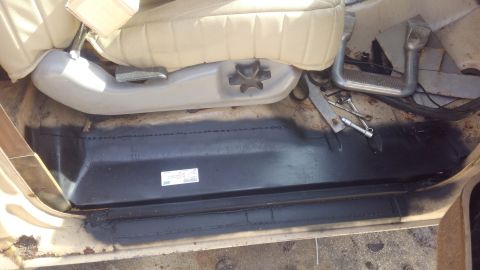 1990 Ford F-250 - The interior floor and seat base of a vehicle are visible, with a label on the black floor panel.