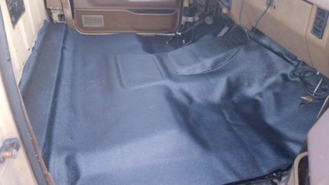 1990 Ford F-250 - The interior floor of a vehicle is covered with new dark vinyl flooring, showing the dashboard and door panel.