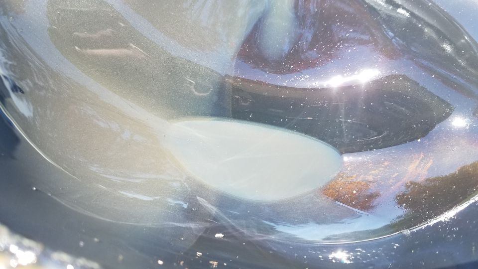 Close-up of a metallic car body panel with a light-colored oval shape, reflecting sunlight
