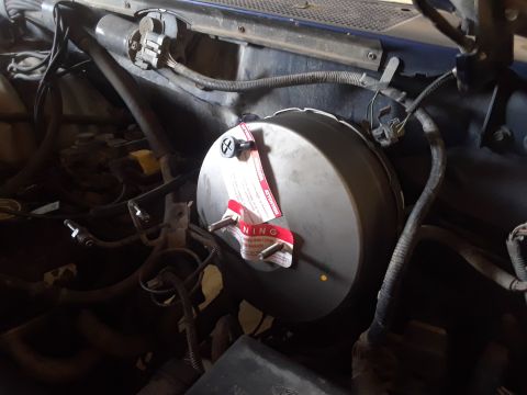 1996 Ford F-350 - Close-up view of a brake booster with attached warning labels and surrounding engine components.