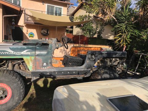 1992 Jeep Wrangler - A green 1992 Jeep Wrangler is shown in a yard, missing its doors and roof, with large off-road tires.