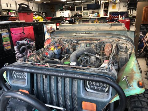 1992 Jeep Wrangler - A 1992 Jeep Wrangler in a garage with its hood open, revealing the engine compartment and aftermarket headlights.