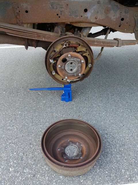 1978 Ford Bronco - Close-up of a rear drum brake assembly and its removed drum, resting on asphalt.