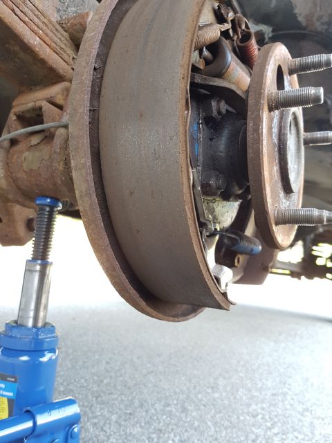 1978 Ford Bronco - Close-up of a vehicle's rear drum brake assembly being supported by a jack.