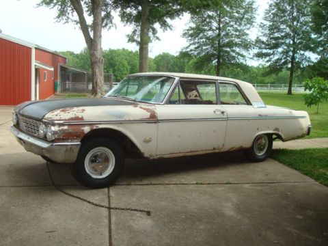 1962 Ford Galaxie - This 1961 Ford sedan shows significant rust and wear, with a contrasting black hood and off-white body.
