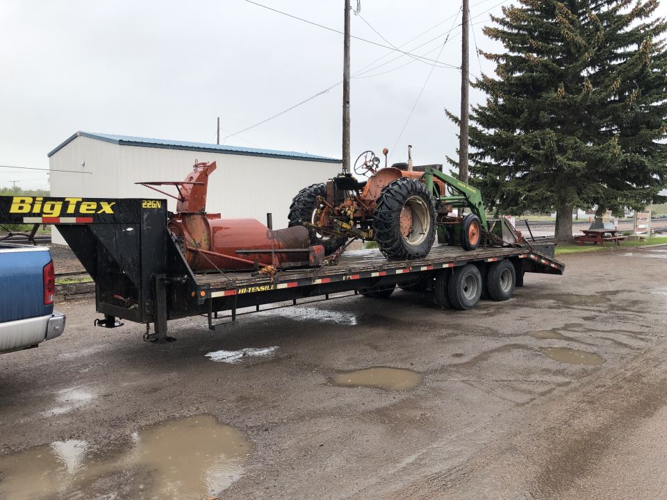 Tractor with front loader and snow blower on a Big Tex trailer being towed by a pickup truck