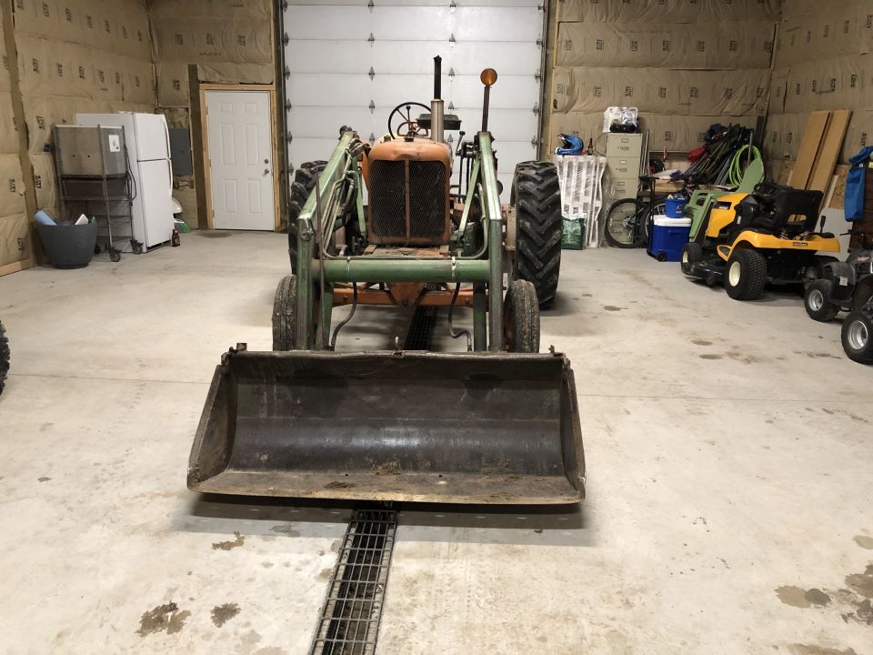 Tractor with front loader in a garage, other lawn equipment visible