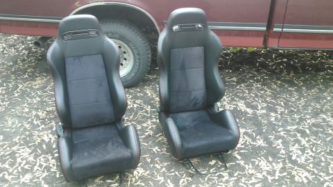 1978 Ford Bronco - Pair of black racing seats with red stitching, positioned outdoors next to a red vehicle.