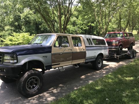 1994 Ford Bronco - A custom Ford F-Series truck tows a Ford Bronco on a trailer, both vehicles are visible from the side.