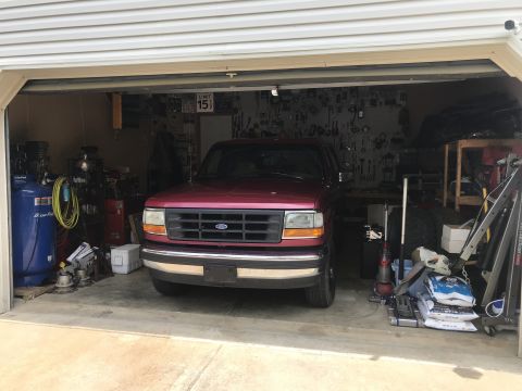 1994 Ford Bronco - A maroon Ford Bronco is parked inside a cluttered garage, viewed from the front.