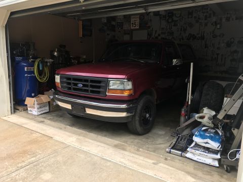 1994 Ford Bronco - A red 1994 Ford Bronco is parked inside a cluttered garage, showing its front 3/4 view.