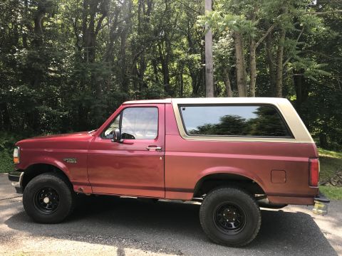 1994 Ford Bronco - Side view of a red and tan 1994 Ford Bronco parked outdoors.