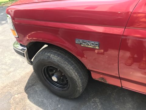 1994 Ford Bronco - Close-up of a red Ford Bronco, highlighting the front fender, wheel, and a 'Bronco' badge.