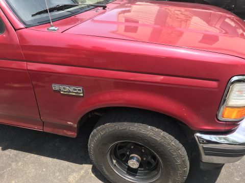1994 Ford Bronco - Close-up of a red 1994 Ford Bronco's front fender, showing the 'Bronco' badge and part of the wheel.