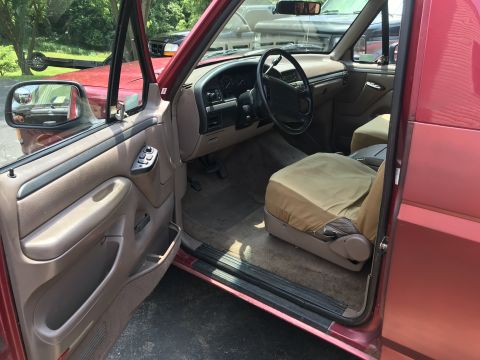 1994 Ford Bronco - The interior of a red SUV is shown, with a seat cover on the driver's seat and a view of the dashboard.