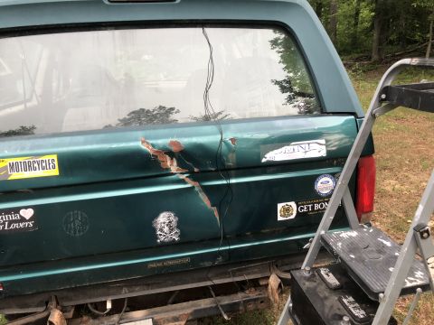 1995 Ford Bronco - Rear view of a green 1995 Ford Bronco showing damage and various stickers on the tailgate.
