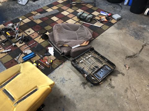 1995 Ford Bronco - A car seat is taken apart on a patterned rug in a garage, surrounded by various tools and equipment.