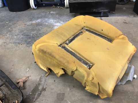 1995 Ford Bronco - A worn car seat cushion lies on a concrete floor, revealing its internal foam structure and damaged edges.