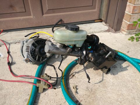 1977 Ford Ranchero - A brake master cylinder and alternator are shown disassembled, resting on a concrete surface.