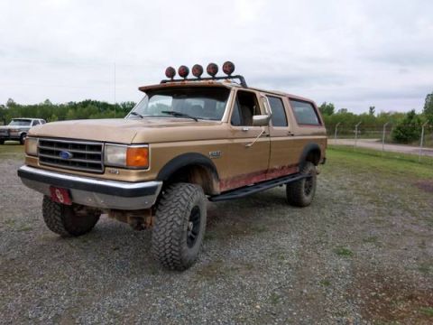 1994 Ford Bronco - This lifted Ford Bronco has aftermarket off-road lights and side steps. A second vehicle is parked behind it.