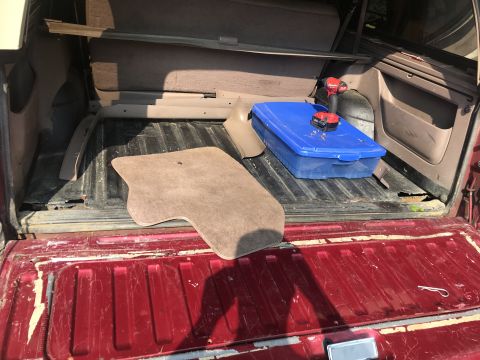 1994 Ford Bronco - Cargo area of a red SUV with tools and floor mats visible inside. The interior trim appears to be partially removed.