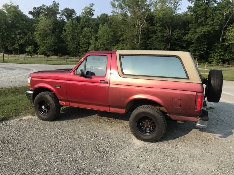 1994 Ford Bronco - This 1994 Ford Bronco features a two-tone paint scheme with a red lower body and a tan removable top.