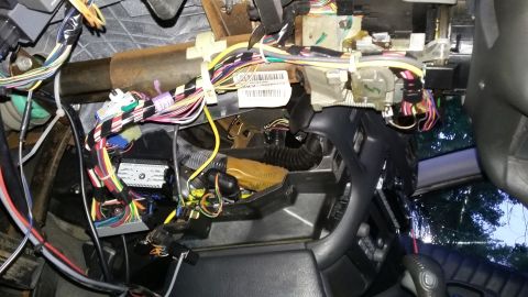 Close-up of a complex wiring harness and electrical components under a vehicle's dashboard