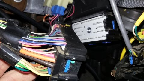 Close-up of a vehicle's complex wiring harness with many colorful wires connected to black and white connector