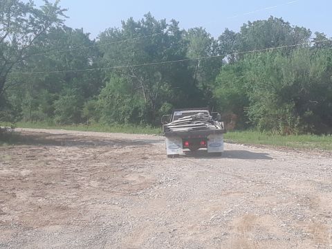 1994 Ford Bronco - A flatbed truck loaded with lumber drives away on a dirt road.