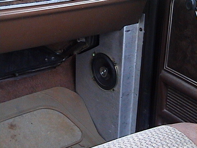 Round speaker mounted in a metal kick panel inside a brown truck cab interior