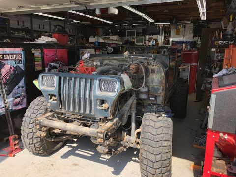 1992 Jeep Wrangler - A disassembled Jeep Wrangler sits in a garage, showing its front end with modified headlights and exposed engine components.