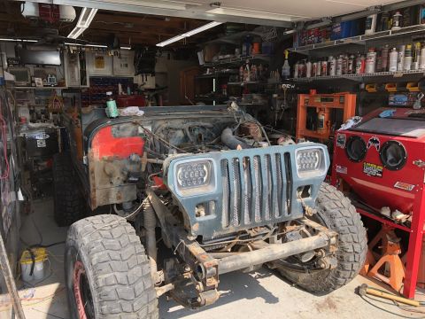 1992 Jeep Wrangler - Front view of a 1992 Jeep Wrangler in a garage, showing its grille and headlights during a tear-down process.